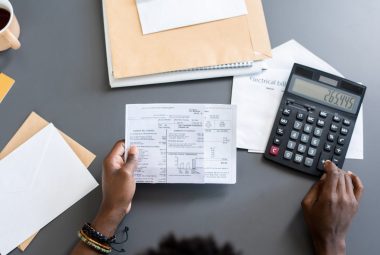 Directly above view of man sitting at gray table with paperwork reviewing line 10100 tax return and making calculations
