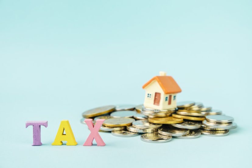 Small house on stack of coins and word TAX. Underused housing tax return deadline symbolism